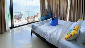 A hotel room with a large bed, a balcony with outdoor seating, and a view of the sea. - Sacaan Tropical Breeze Resort (Sogod)
