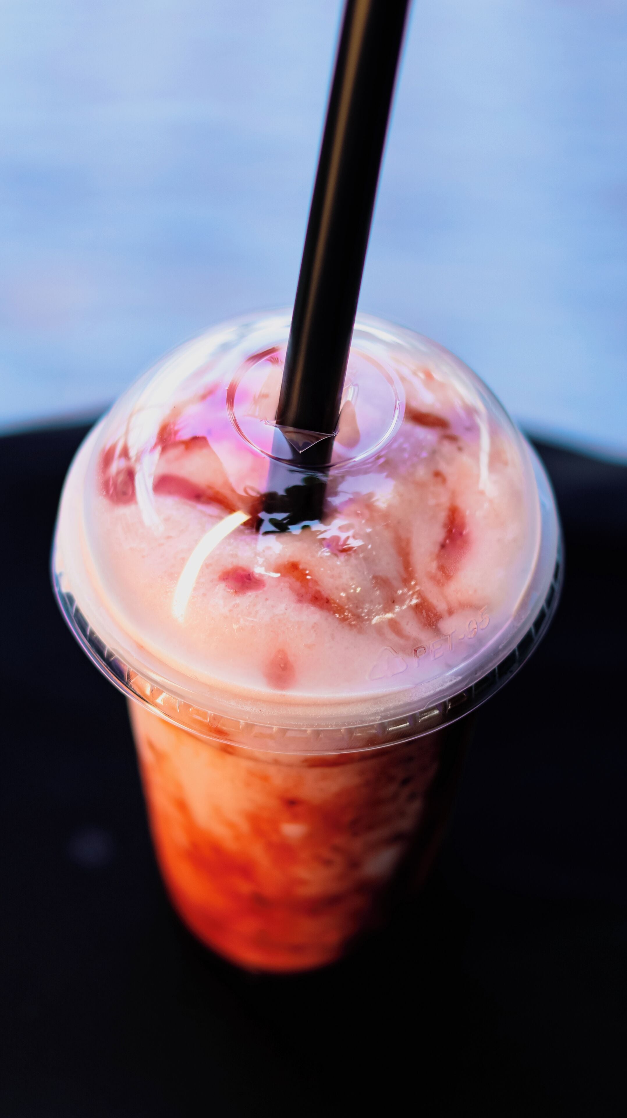 A clear plastic cup with a straw, containing a beverage with ice cubes and a pinkish liquid.