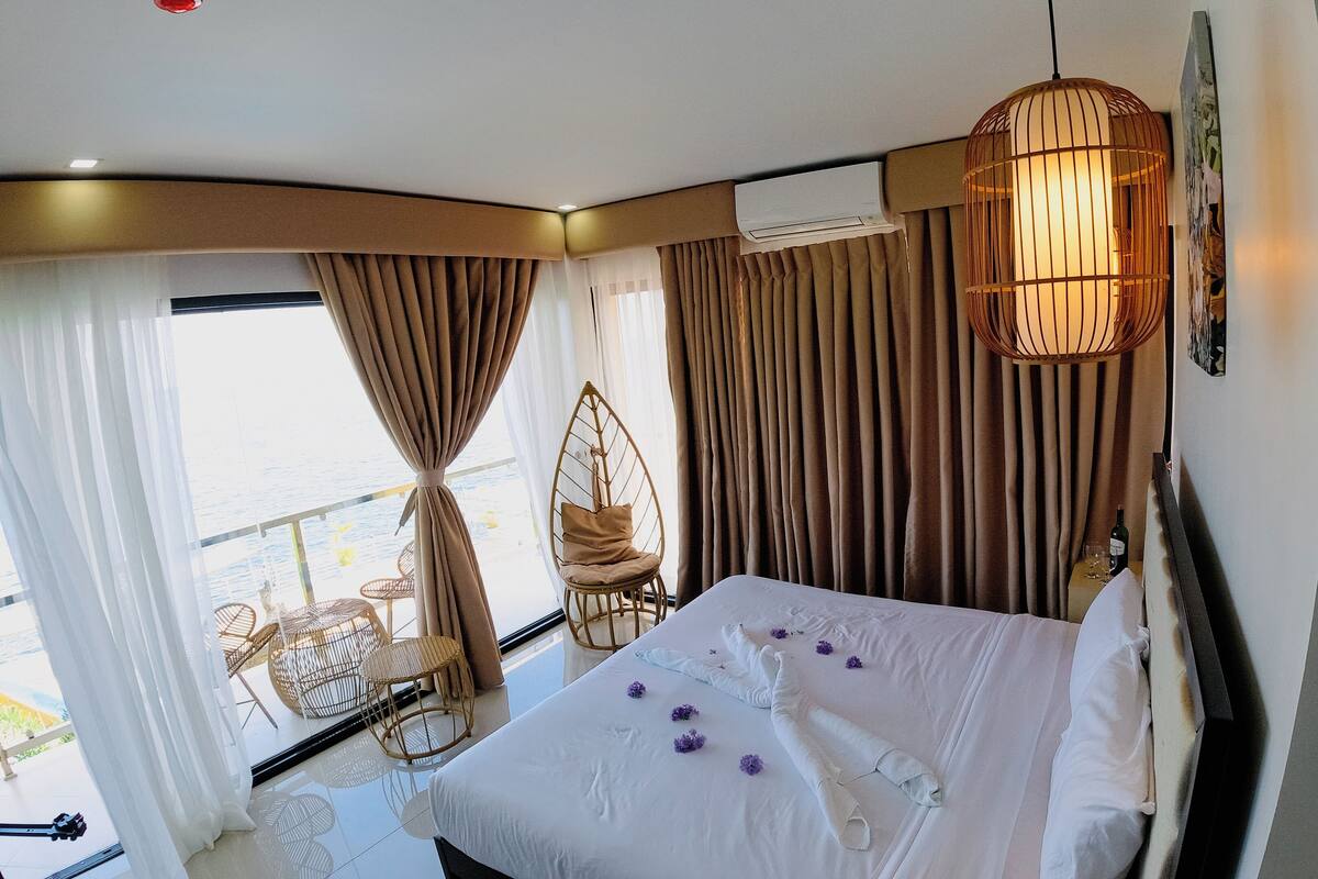 A hotel room with a bed, curtains, a hanging chair, and a balcony with wicker furniture.