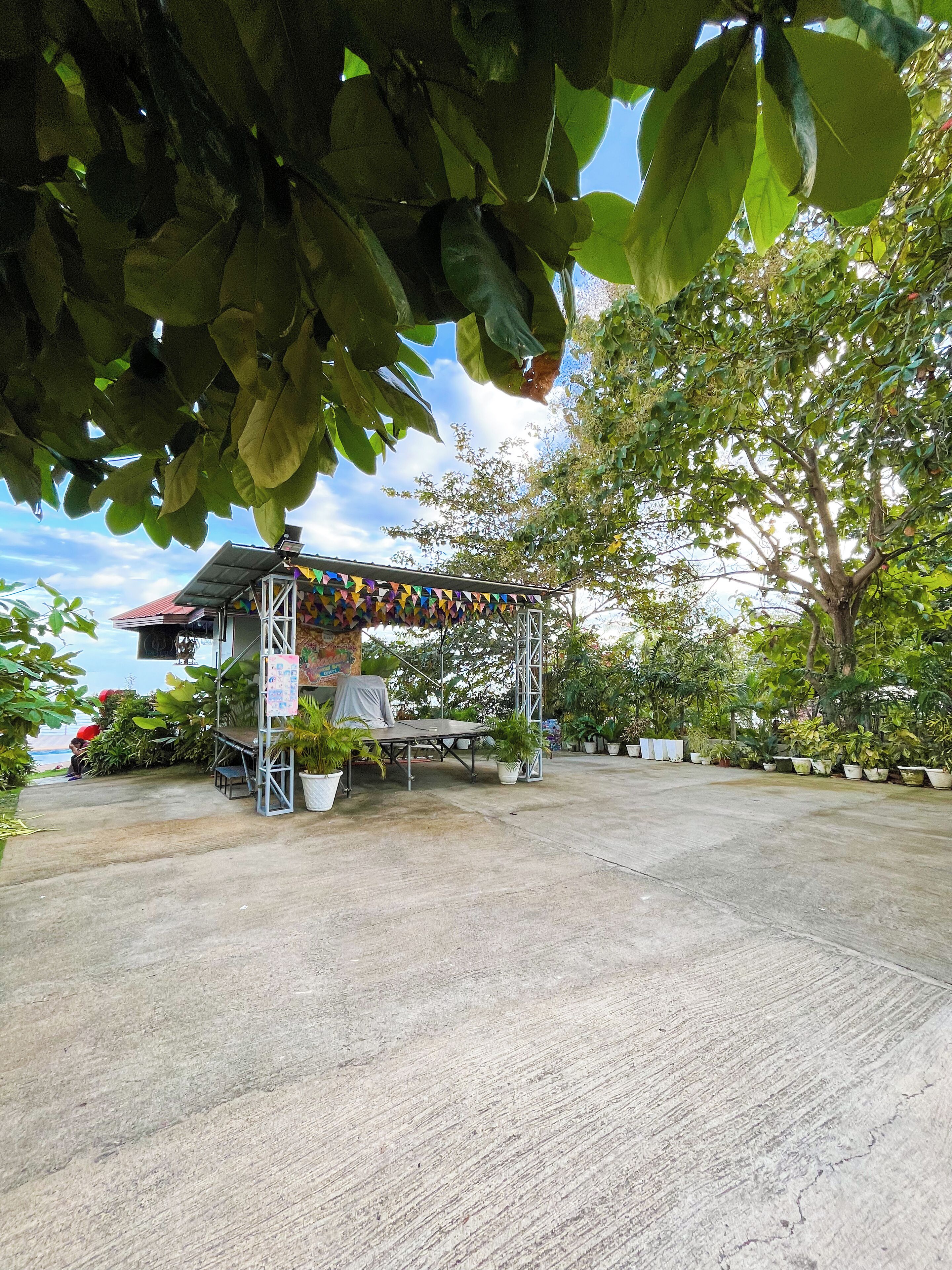 A covered outdoor area with a stage, potted plants, and a metal structure.