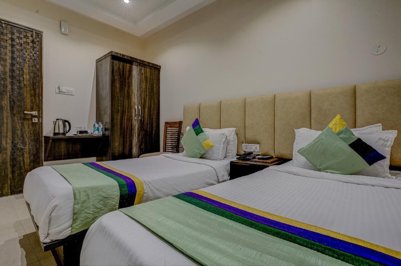 A hotel room with two beds, a wardrobe, a desk with a kettle, and a nightstand with a phone.
