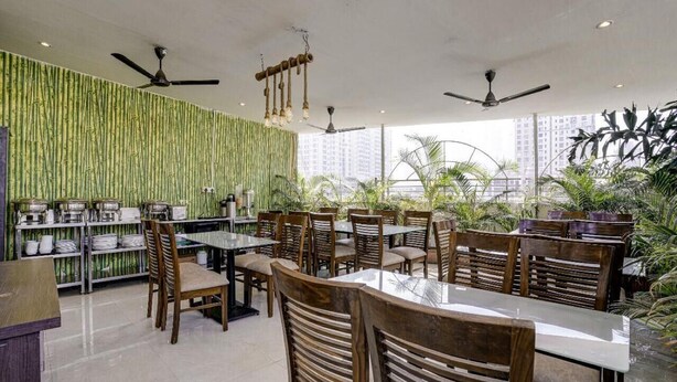 Restaurante con decoración de pared de bambú, varias mesas y sillas, ventiladores de techo y grandes ventanales con vistas a un paisaje urbano.