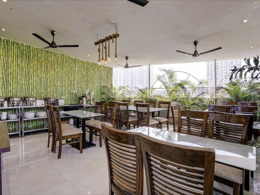 Restaurante con decoración de pared de bambú, varias mesas y sillas, ventiladores de techo y grandes ventanales con vistas a un paisaje urbano.