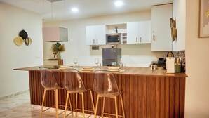 Una cocina moderna con una isla de madera, taburetes de bar, armarios blancos y un microondas.