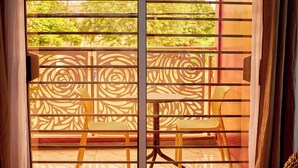 Una habitación con vistas a través de una ventana con un panel decorativo, una cama y una silla.