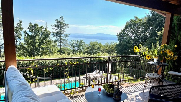 A balcony with a view of a lake and mountains, a pool, and outdoor furniture.