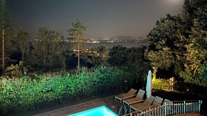 A nighttime view of a pool area with lounge chairs and a moon in the sky.