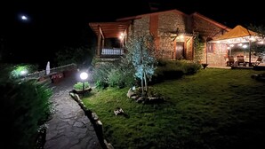 A stone building with a wooden porch and outdoor seating area, surrounded by well-lit landscaping.