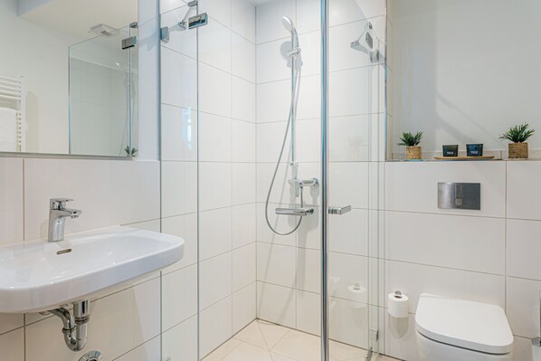Un baño moderno con ducha de vidrio, lavamanos blanco y retrete.