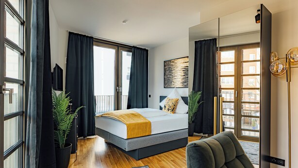A modern bedroom with a bed, a large window, and a view of the city. - Urban Heaven Aparthotel (Hamburg)