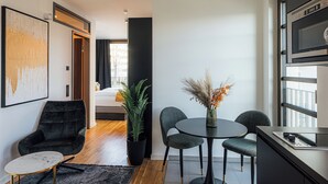 A modern hotel room with a dining area, a black armchair, a small table, and a potted plant. - Urban Heaven Aparthotel (Hamburg)