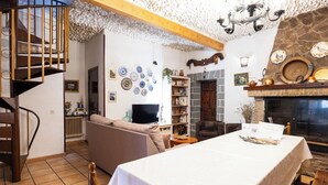 A cozy living room with a sofa, a dining table, and a fireplace. There is a bookshelf and a TV in the room.