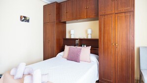 A bedroom with a bed, wooden wardrobe, and a small table with a lamp.