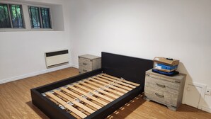 A bedroom with a wooden bed frame, a nightstand, a dresser, and a window with blinds.