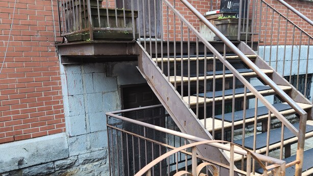 A set of outdoor metal stairs with a metal railing, leading to a brick building with a door and a window.