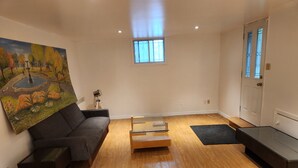 A modern living room with a dark grey sofa, a glass-top coffee table, and a painting of a park scene on the wall.