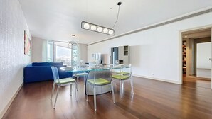 Una sala de estar moderna con una mesa de comedor de cristal, sillas traslúcidas y un sofá azul.