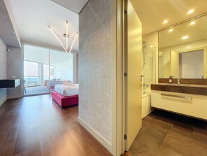 Una habitación de hotel moderna con una cama grande, un baño con un espejo amplio y un balcón con vista al océano.