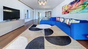 Una sala de estar moderna con un televisor de pantalla plana grande, un sofá modular azul, un tapete estampado y un cuadro abstracto colorido en la pared.