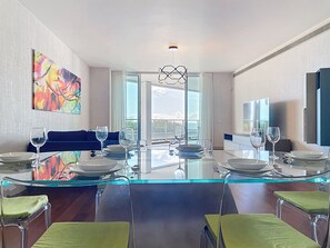 Un comedor moderno con una mesa de vidrio, sillas con cojines verdes y vistas al exterior.