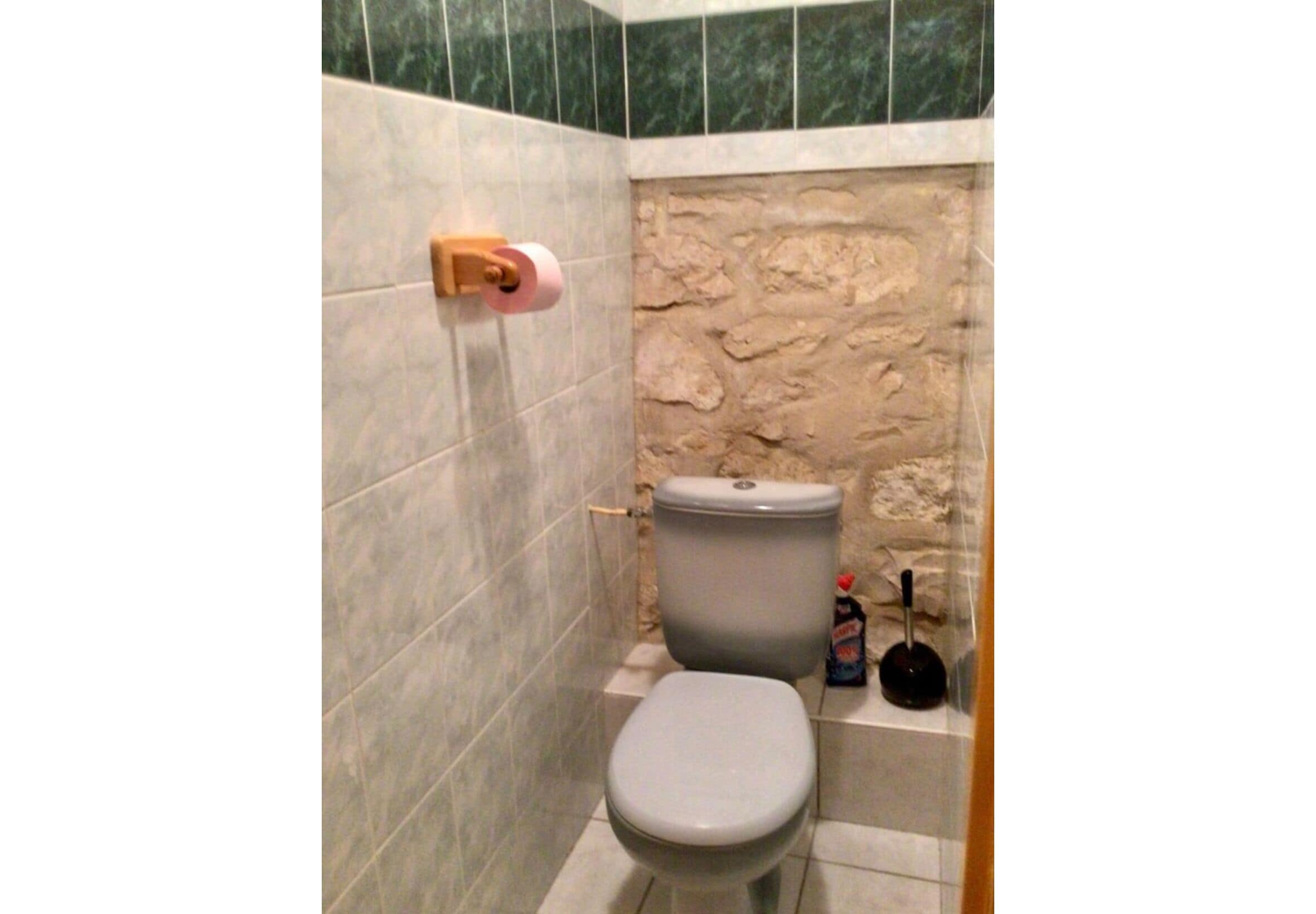 A bathroom with a toilet, a stone wall, and a tiled floor.