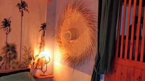 Een kamer met een bed, een wandlamp, een decoratie van een pauwenveer en een raam met verticale jaloezieën.