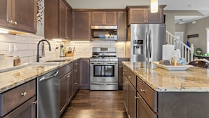 A modern kitchen with wooden cabinets, stainless steel appliances, and a granite countertop.