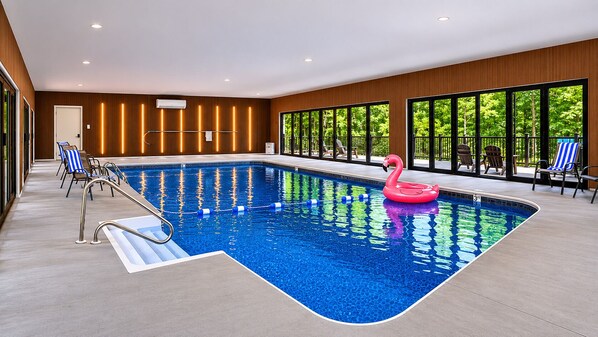 A swimming pool with a pink flamingo float, lounge chairs, and a view of greenery through large windows. - LUX Heated Pool, Pickleball, Hot Tub Sauna, Arcade (Canadensis)
