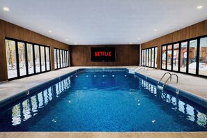 An indoor swimming pool with a Netflix screen, wooden walls, and large windows. - LUX Heated Pool, Pickleball, Hot Tub Sauna, Arcade (Canadensis)
