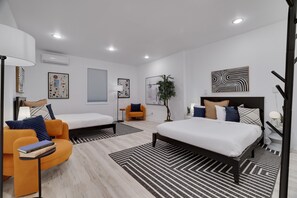 A modern bedroom with a large bed, a sofa, and a chair. There is a window with blinds, a plant, and artwork on the walls. - LUX Heated Pool, Pickleball, Hot Tub Sauna, Arcade (Canadensis)
