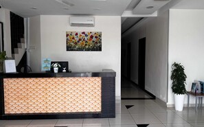 A reception area with a patterned reception desk, an air conditioning unit, a floral painting, and a potted plant. - OYO 91119 Hotel D Lima Inn (Langkawi)