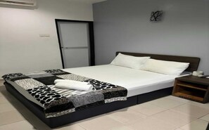A neatly made bed with a patterned bedspread and pillows, a wooden nightstand with a remote control, and a plain wall with a simple artwork.