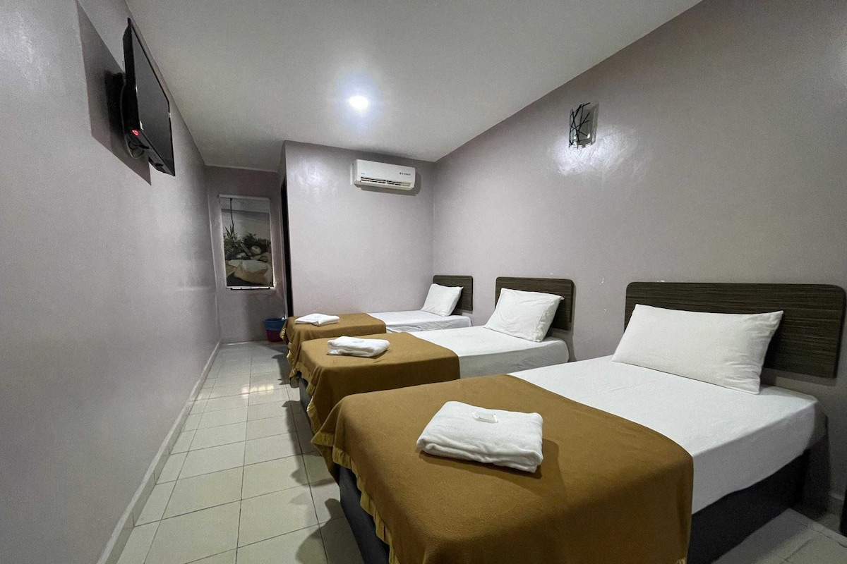 A hotel room with three single beds, a flat-screen TV mounted on the wall, and a window with a view of the outdoors.
