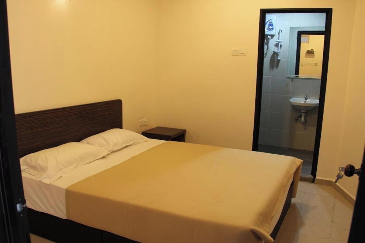 A single bed with a wooden headboard, a bedside table, and a bathroom visible through a glass door.