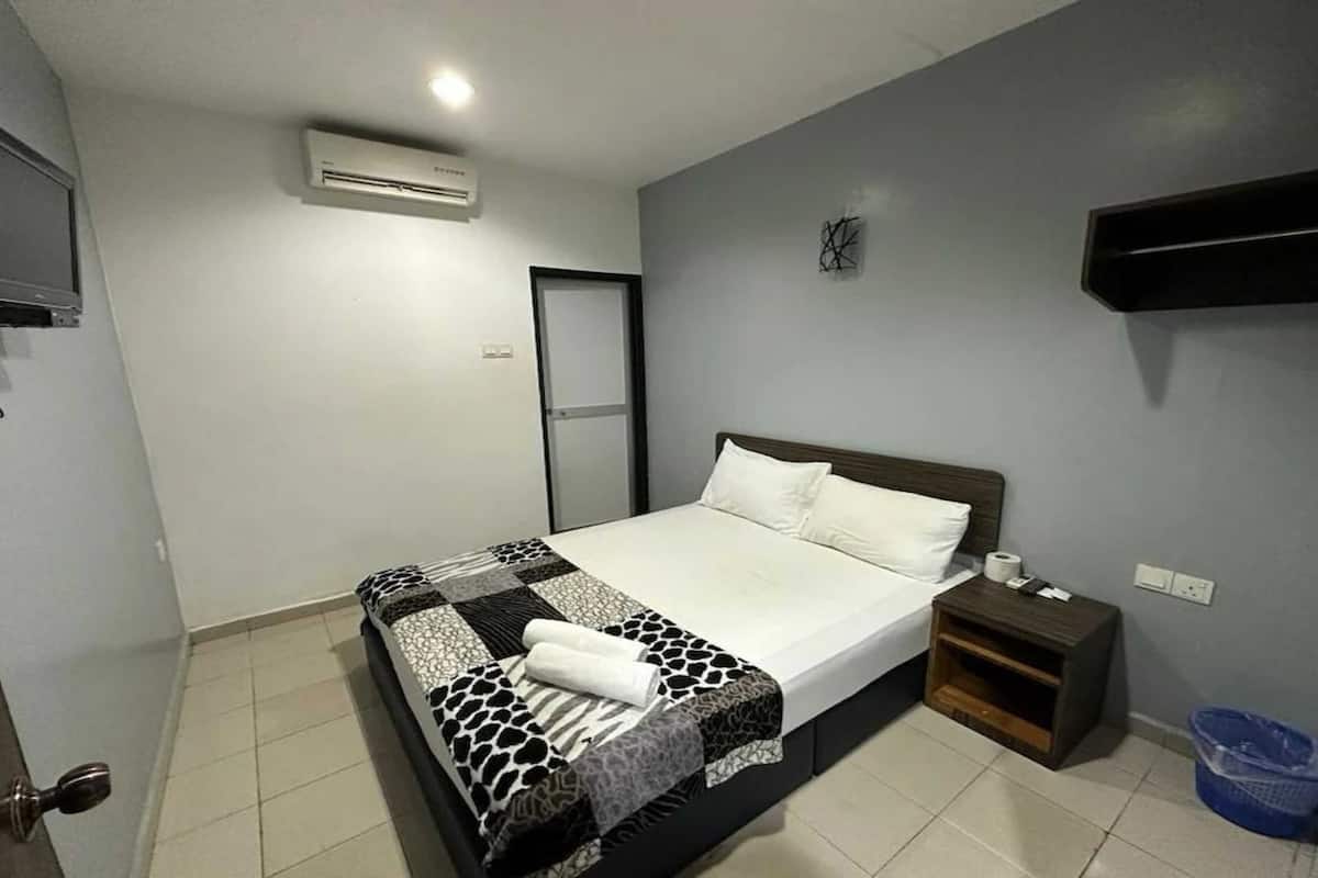 A neatly made bed with a patterned bedspread, a bedside table with a lamp, and a wall-mounted TV.