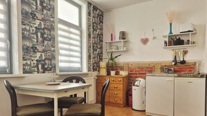 Cocina compacta con mesa, sillas, refrigerador y ventana con persianas.