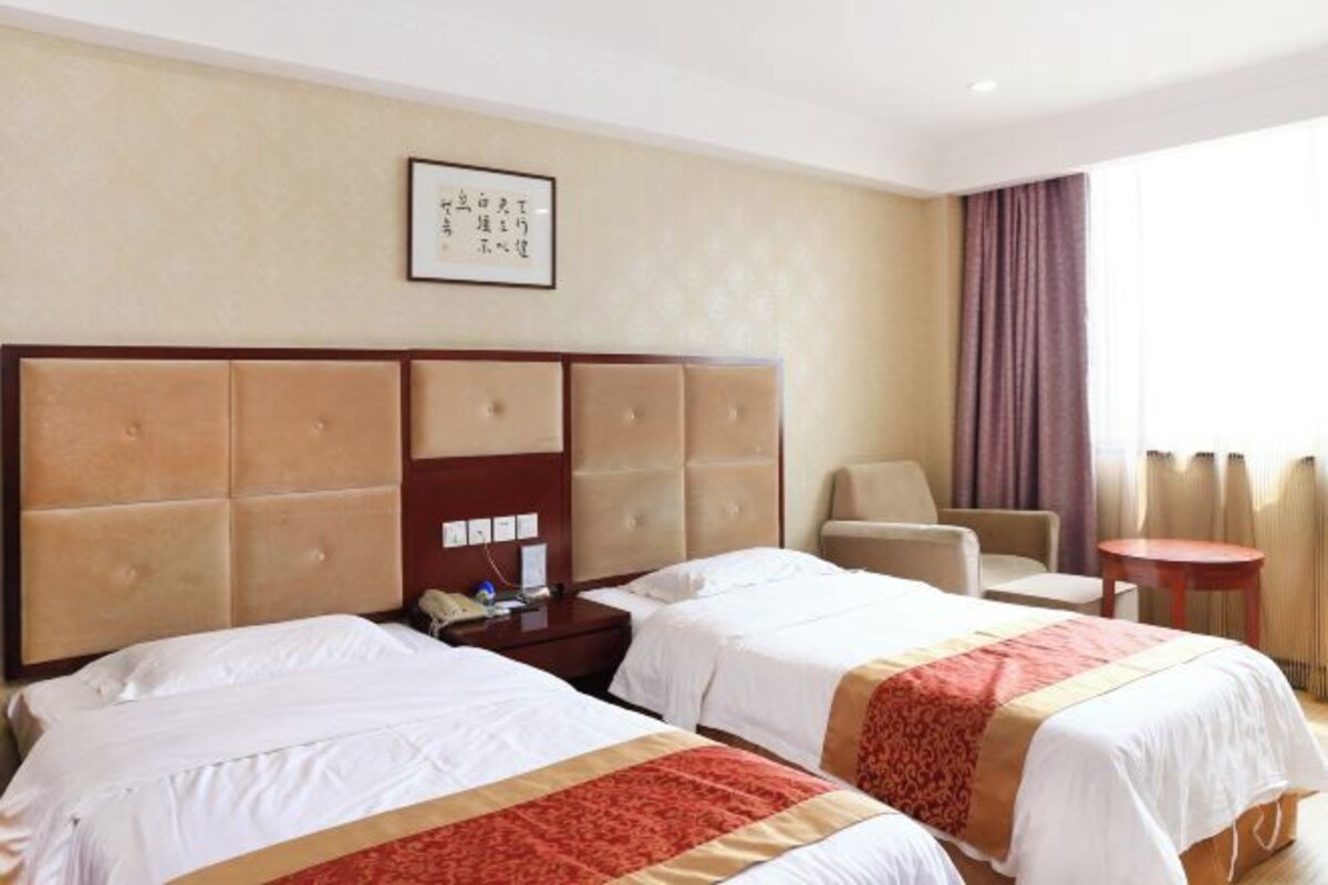Une chambre d’hôtel avec deux lits, une tête de lit en bois, une petite table, une chaise et une fenêtre avec des rideaux.