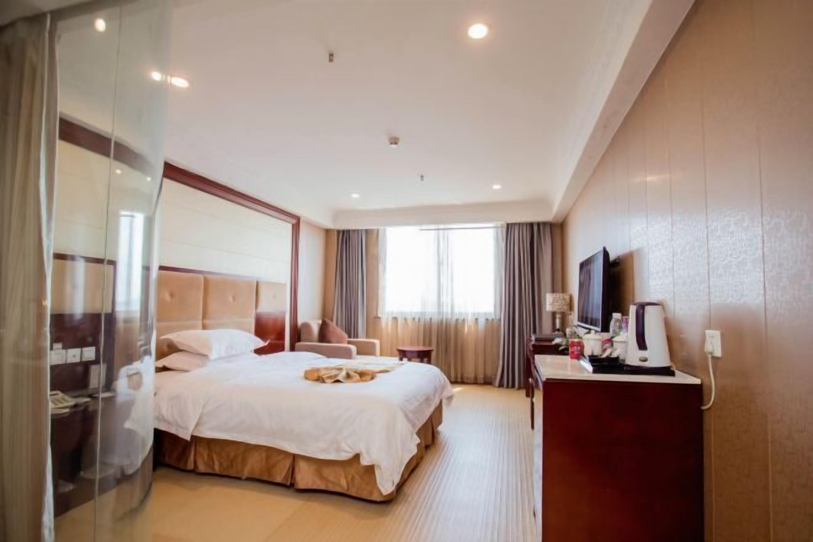 Une chambre d’hôtel avec un grand lit, un bureau avec une télévision et une cloison en verre.