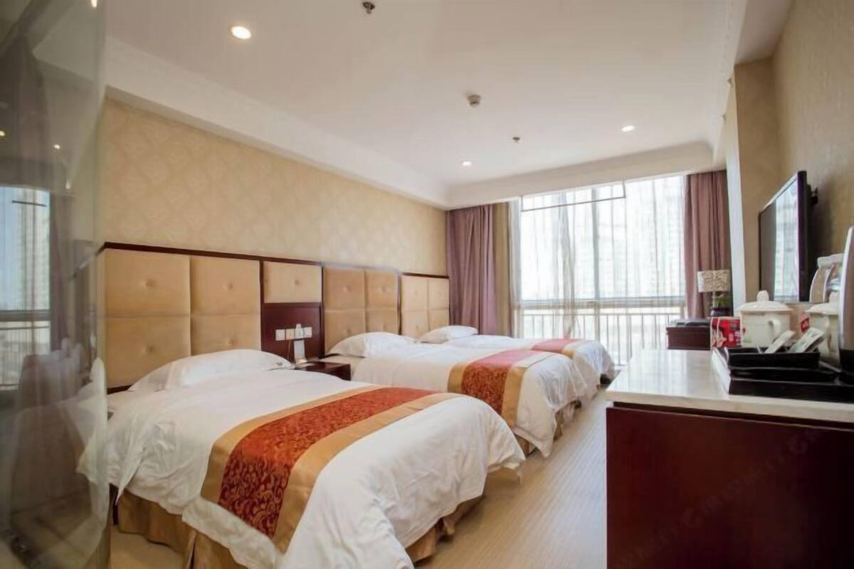 A hotel room with two beds, a desk, and a large window.