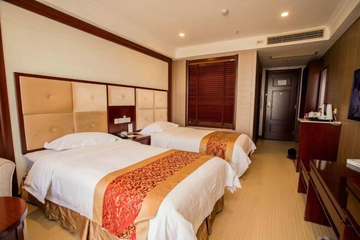 A hotel room with two beds, a desk, a chair, a television, and a door leading to another room.