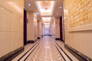 A hotel corridor with a patterned floor, recessed lighting, and a wall with a textured design.