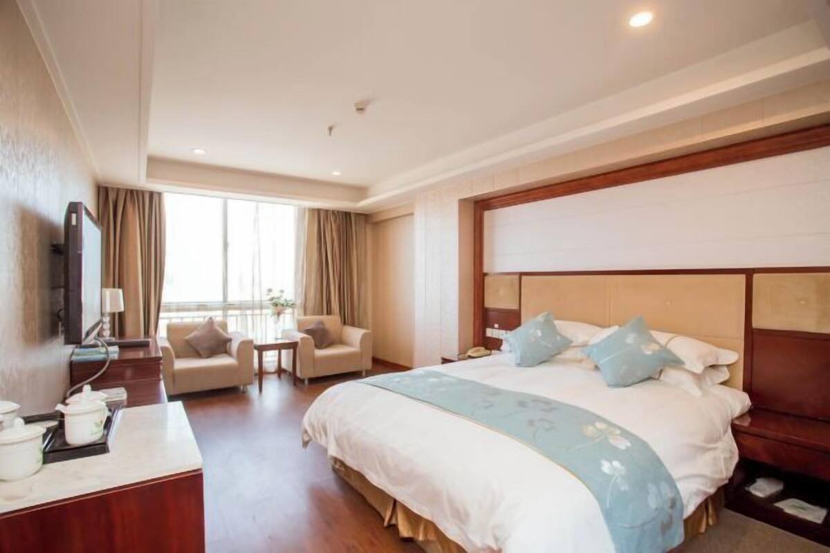 A hotel room with a large bed, a desk with a telephone, a chair, and a window with curtains.