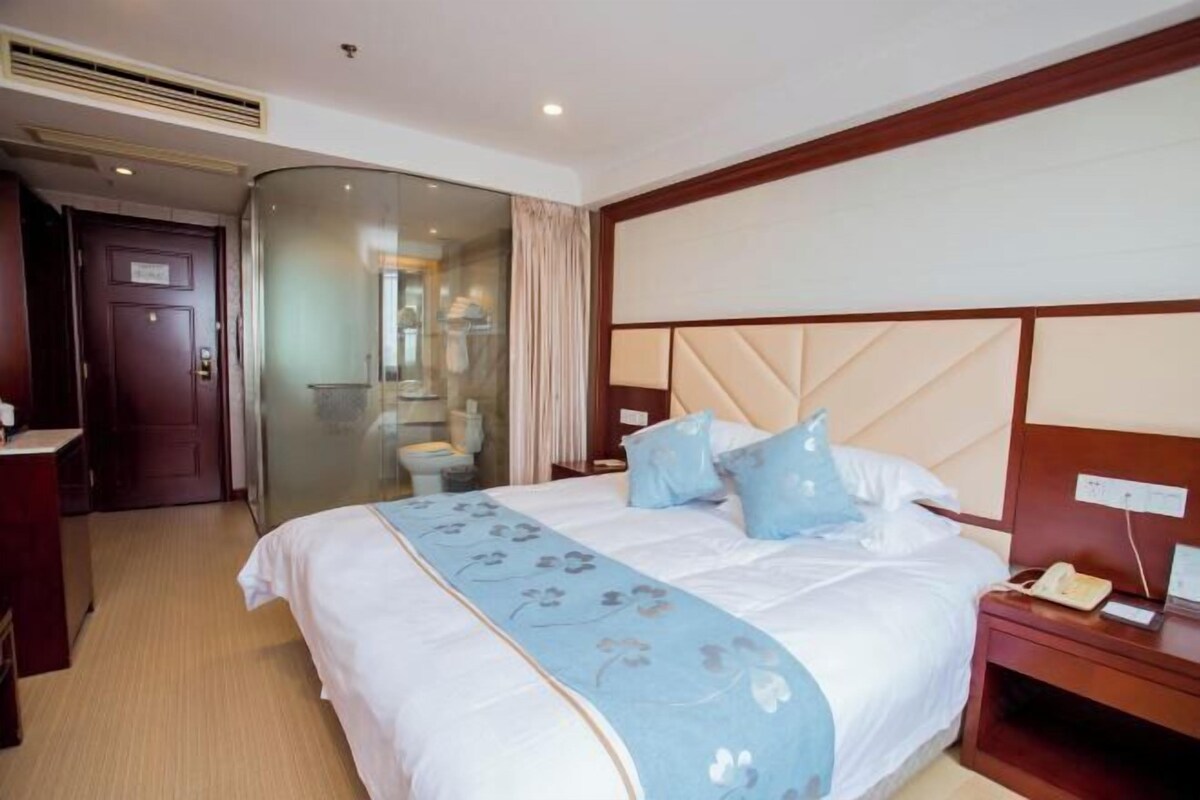 Een hotelkamer met een bed, nachtkastje en een glazen scheiding die de kamer van de badkamer scheidt.