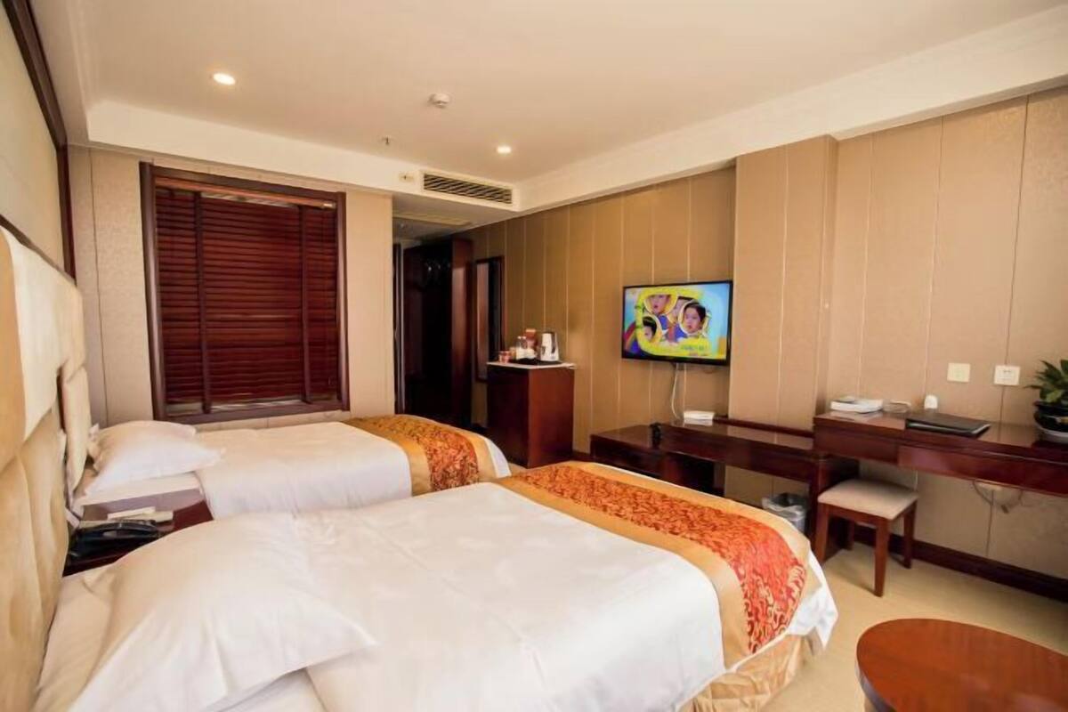 A hotel room with two beds, a desk, a television, and a small seating area.