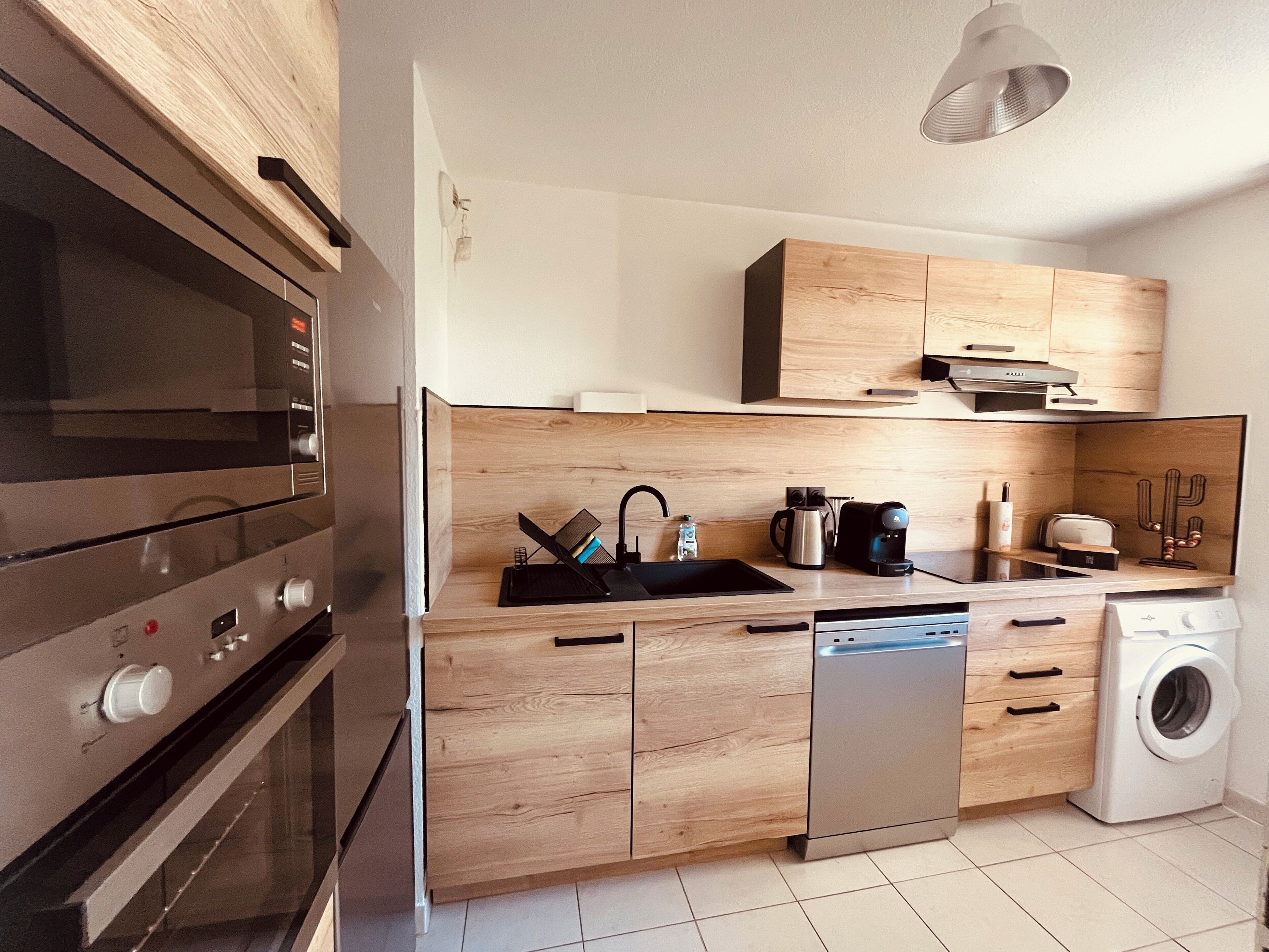 A compact kitchen with wooden cabinets, a built-in oven, a dishwasher, and a washing machine.