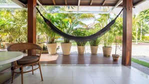 Ein überdachter Patio-Bereich mit einem Korbstuhl, einem Tisch und mehreren Blumentöpfen.