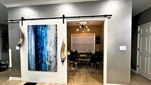 A room with a sliding door leading to a dining area, a chandelier, and a large abstract painting. - Luxe 4 Bed ATL Retreat - Pool, Fire, Sauna, Theater (Atlanta)