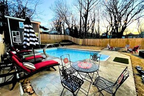 A backyard with a swimming pool, lounge chairs, a table with chairs, and a wooden fence. - Luxe 4 Bed ATL Retreat - Pool, Fire, Sauna, Theater (Atlanta)