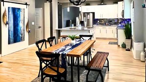 A modern kitchen with white cabinets, stainless steel appliances, and a wooden dining table with chairs. - Luxe 4 Bed ATL Retreat - Pool, Fire, Sauna, Theater (Atlanta)