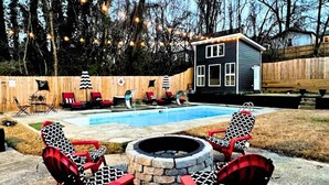 A backyard with a swimming pool, a small deck, and outdoor seating with red and black patterned chairs. - Luxe 4 Bed ATL Retreat - Pool, Fire, Sauna, Theater (Atlanta)
